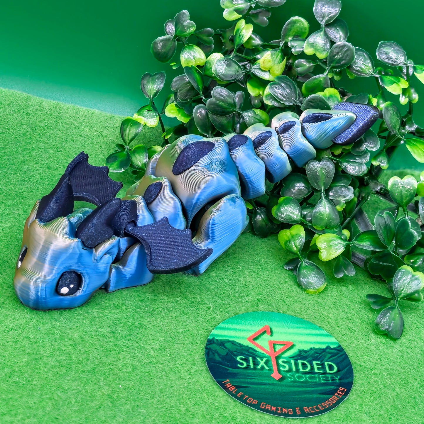 3D printed articulated baby dragon figurine for tabletop gaming – perfect Dungeons & Dragons gift, RPG accessory, and fantasy desk decor. Multi‑colour PLA dragon with movable wings and tail for fidget play during D&D, Pathfinder, and TTRPG campaigns. Ideal gamer gift for Dungeon Masters, dice collectors, and fantasy enthusiasts – handcrafted by Six Sided Society in Coventry, UK.