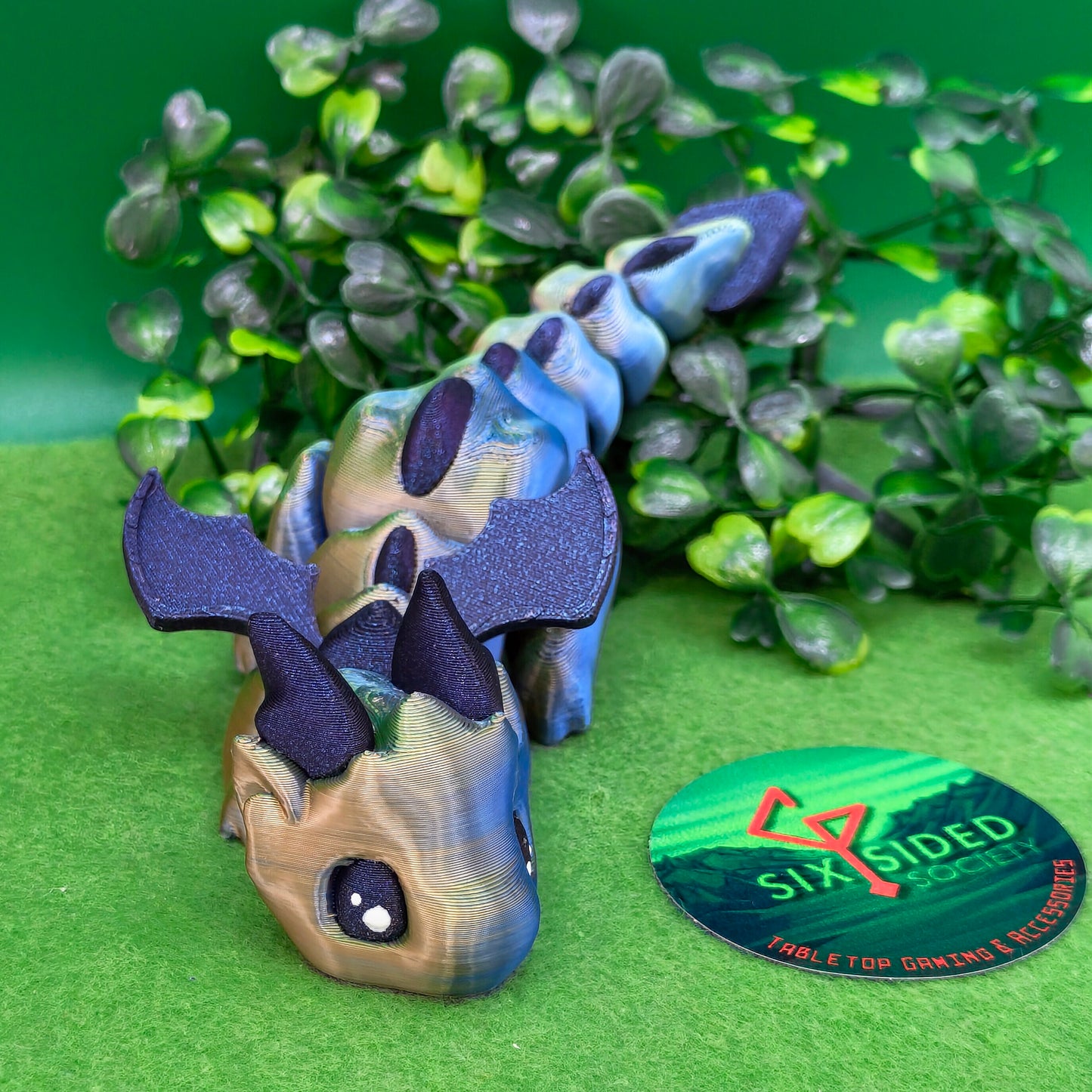 3D printed articulated baby dragon figurine for tabletop gaming – perfect Dungeons & Dragons gift, RPG accessory, and fantasy desk decor. Multi‑colour PLA dragon with movable wings and tail for fidget play during D&D, Pathfinder, and TTRPG campaigns. Ideal gamer gift for Dungeon Masters, dice collectors, and fantasy enthusiasts – handcrafted by Six Sided Society in Coventry, UK.