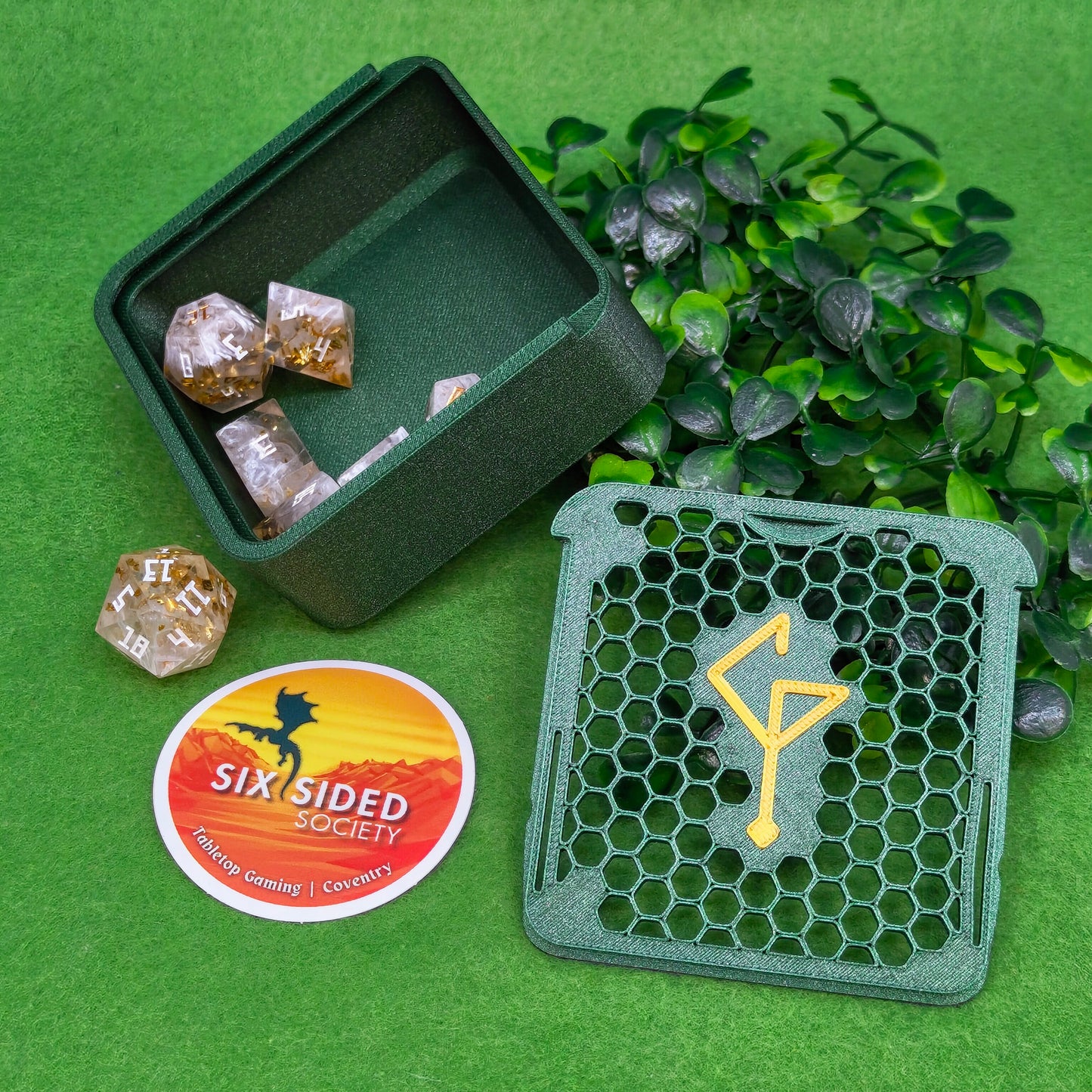 Green dice case with dice, green diegetic standee, and Six Sided Society sticker on a green background.3D-printed D20 dice trinket box by Six Sided Society, tabletop gaming storage for Dungeons & Dragons, RPG dice organizer, eco-friendly gift box for dice collectors and dungeon masters, perfect accessory for board games and role-playing sessions.