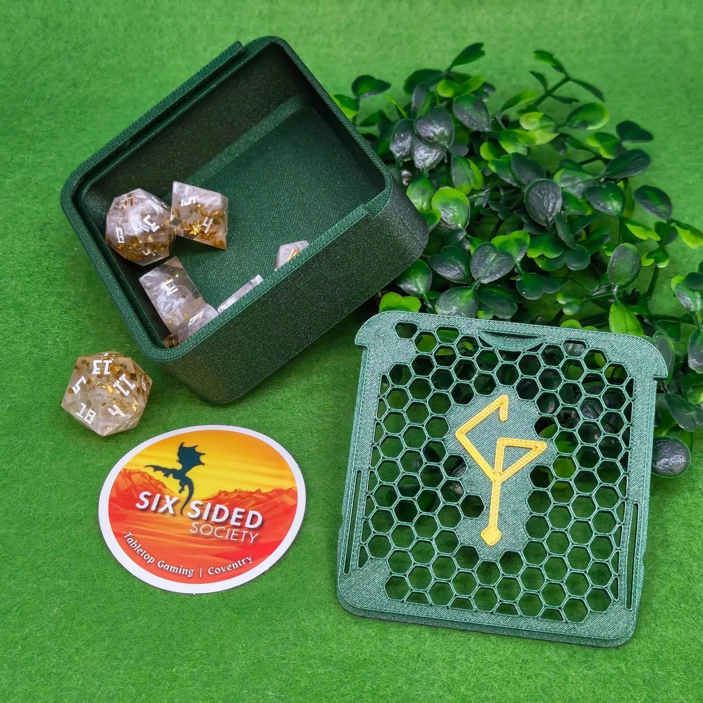 Green dice case with dice, green diegetic standee, and Six Sided Society sticker on a green background.3D-printed D20 dice trinket box by Six Sided Society, tabletop gaming storage for Dungeons & Dragons, RPG dice organizer, eco-friendly gift box for dice collectors and dungeon masters, perfect accessory for board games and role-playing sessions.