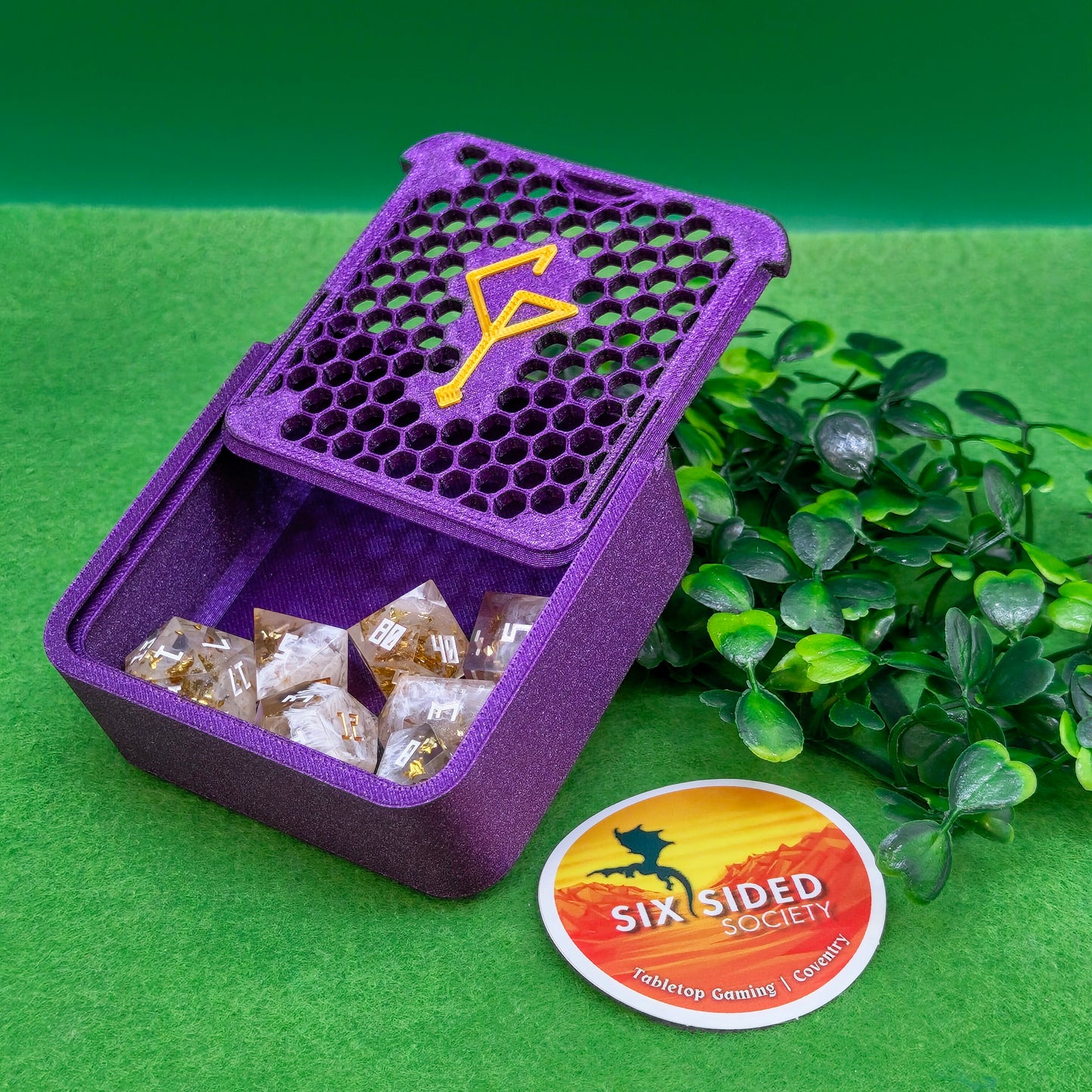 Purple dice container with dice and a 'Six Sided Society' logo on a green background. 3D-printed D20 dice trinket box by Six Sided Society, tabletop gaming storage for Dungeons & Dragons, RPG dice organizer, eco-friendly gift box for dice collectors and dungeon masters, perfect accessory for board games and role-playing sessions
