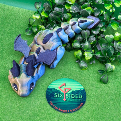 3D printed articulated baby dragon figurine for tabletop gaming – perfect Dungeons & Dragons gift, RPG accessory, and fantasy desk decor. Multi‑colour PLA dragon with movable wings and tail for fidget play during D&D, Pathfinder, and TTRPG campaigns. Ideal gamer gift for Dungeon Masters, dice collectors, and fantasy enthusiasts – handcrafted by Six Sided Society in Coventry, UK.