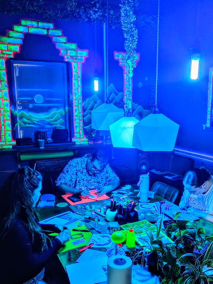 People sitting around a table in a room with UV lighting and decorations.