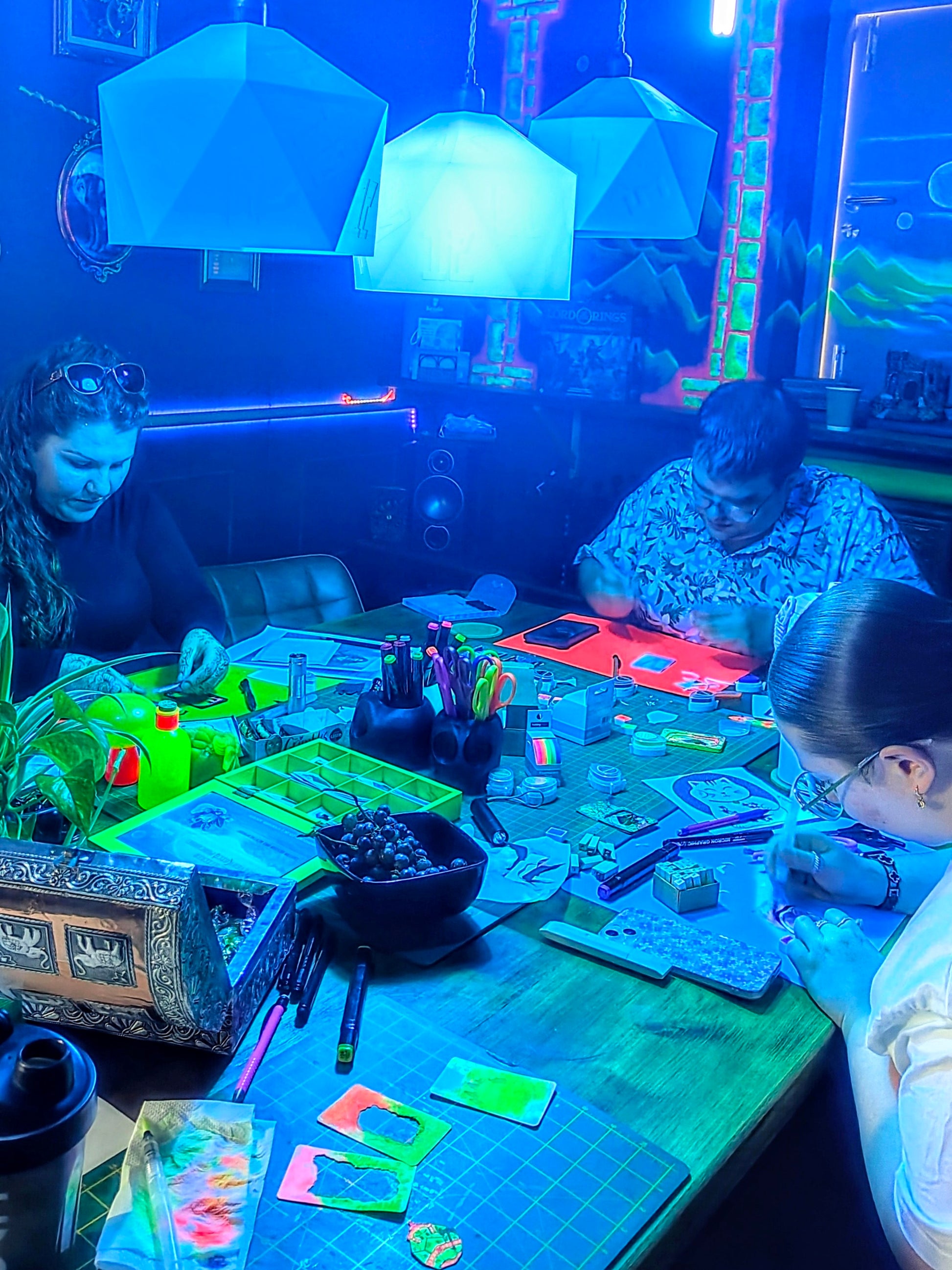 People crafting in a dimly lit room with colorful lights.
