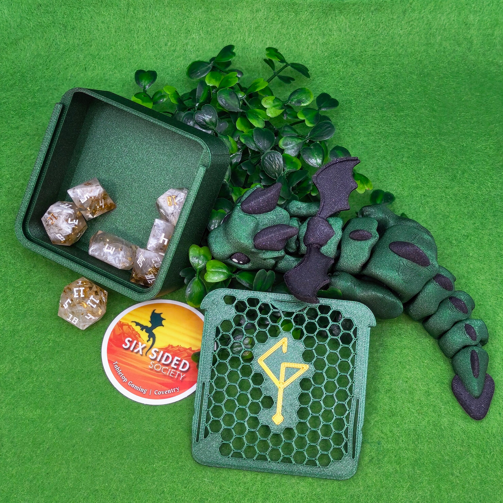 Green dragon toy with dice and a box on a green background. 3D-printed D20 dice trinket box by Six Sided Society, tabletop gaming storage for Dungeons & Dragons, RPG dice organizer, eco-friendly gift box for dice collectors and dungeon masters, perfect accessory for board games and role-playing sessions