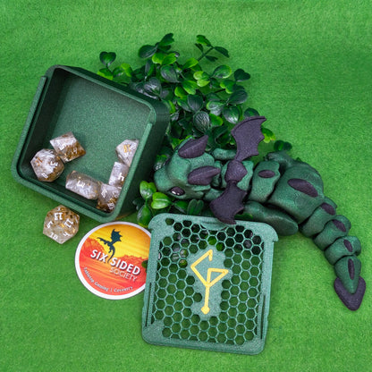 Green dragon toy with dice and a box on a green background. 3D-printed D20 dice trinket box by Six Sided Society, tabletop gaming storage for Dungeons & Dragons, RPG dice organizer, eco-friendly gift box for dice collectors and dungeon masters, perfect accessory for board games and role-playing sessions